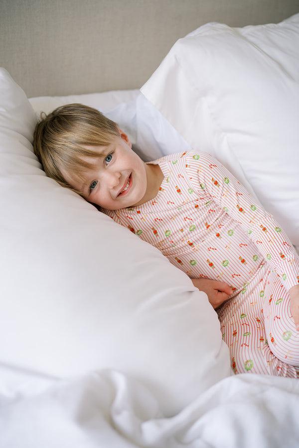 Child in pajamas lying on a bed with white bedding