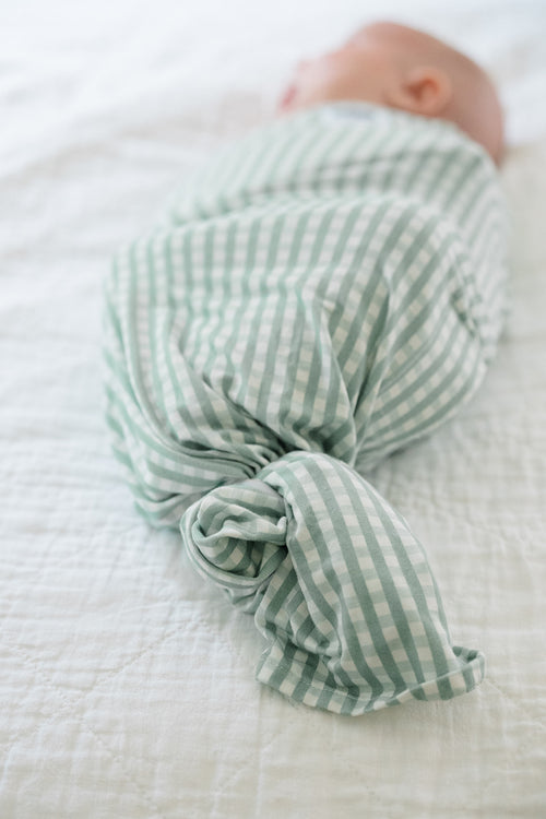 Newborn baby swaddled in a green and white striped blanket on a white surface
